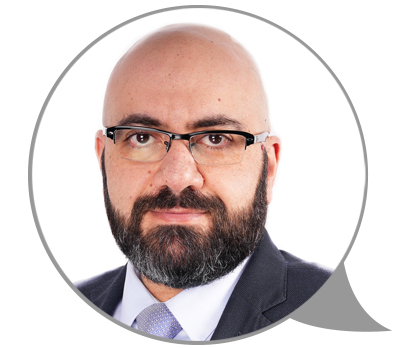 Imad_Alainachi_2 Un homme avec des lunettes et une barbe vêtu d’un costume sourit. Photo : Dre Imad Alainachi