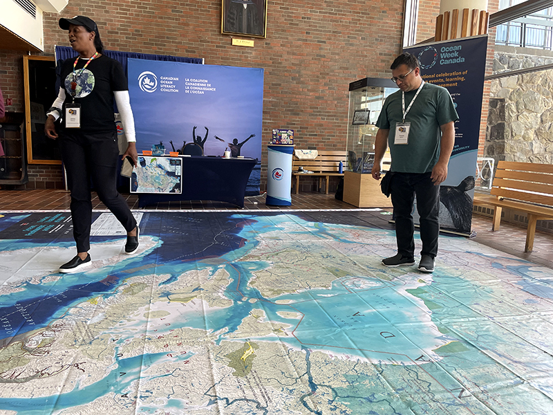 Deux personnes portant des badges dans une salle de conférence marchant sur une grande carte montrant les réseaux d'eau du Canada.