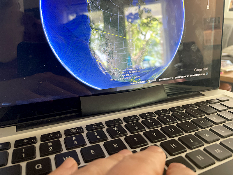 Clavier d'ordinateur portable avec les doigts près des lettres E-R-T-H, et image GoogleEarth de la planète affichée à l'écran.